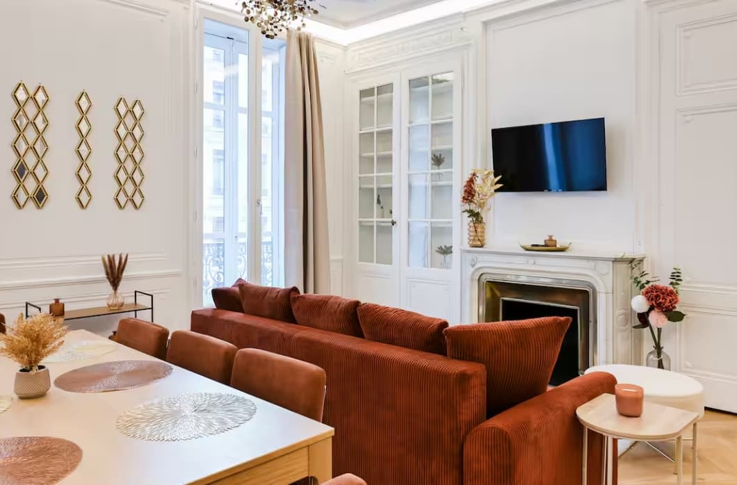 Salon blanc élégant avec canapé en velours terracotta, cheminée et coin salle à manger.