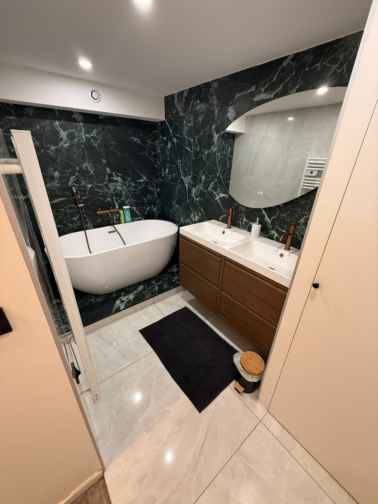 Salle de bain moderne avec baignoire blanche, double vasque en bois et marbre vert.
