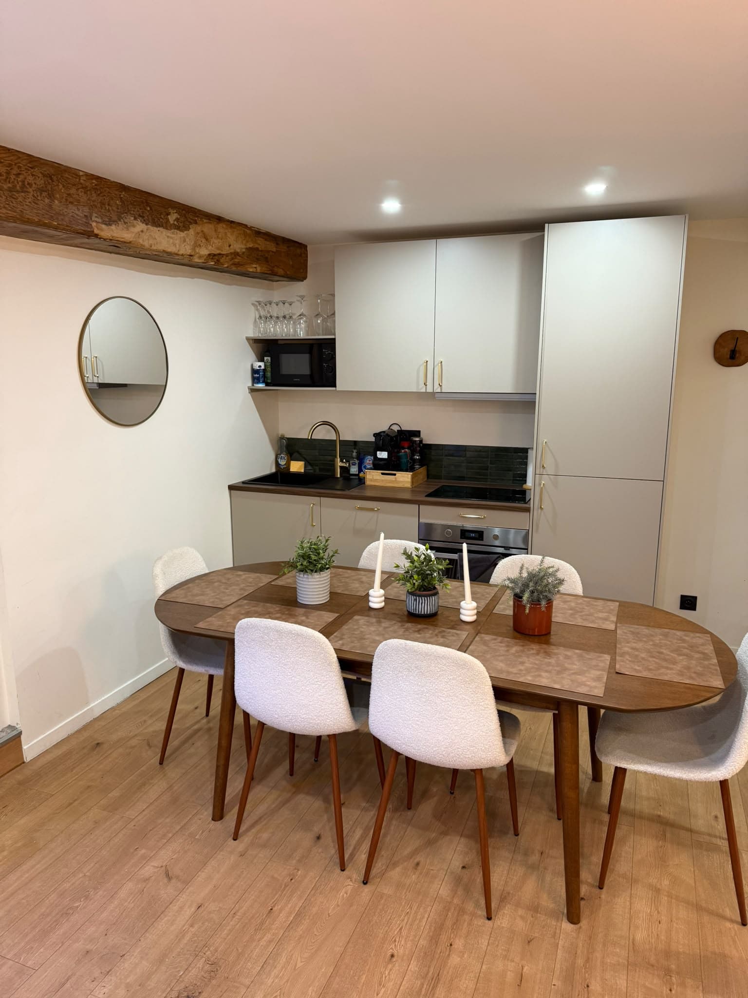 Table à manger en bois avec chaises blanches devant une petite cuisine moderne équipée.